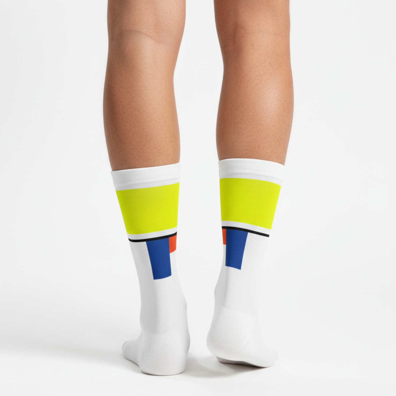 Weiße Radsocken mit neongelbem Bündchen und grafischen Farbdetails in Blau und Orange, getragen von hinten an den Unterschenkeln einer Person vor hellem Studiohintergrund.