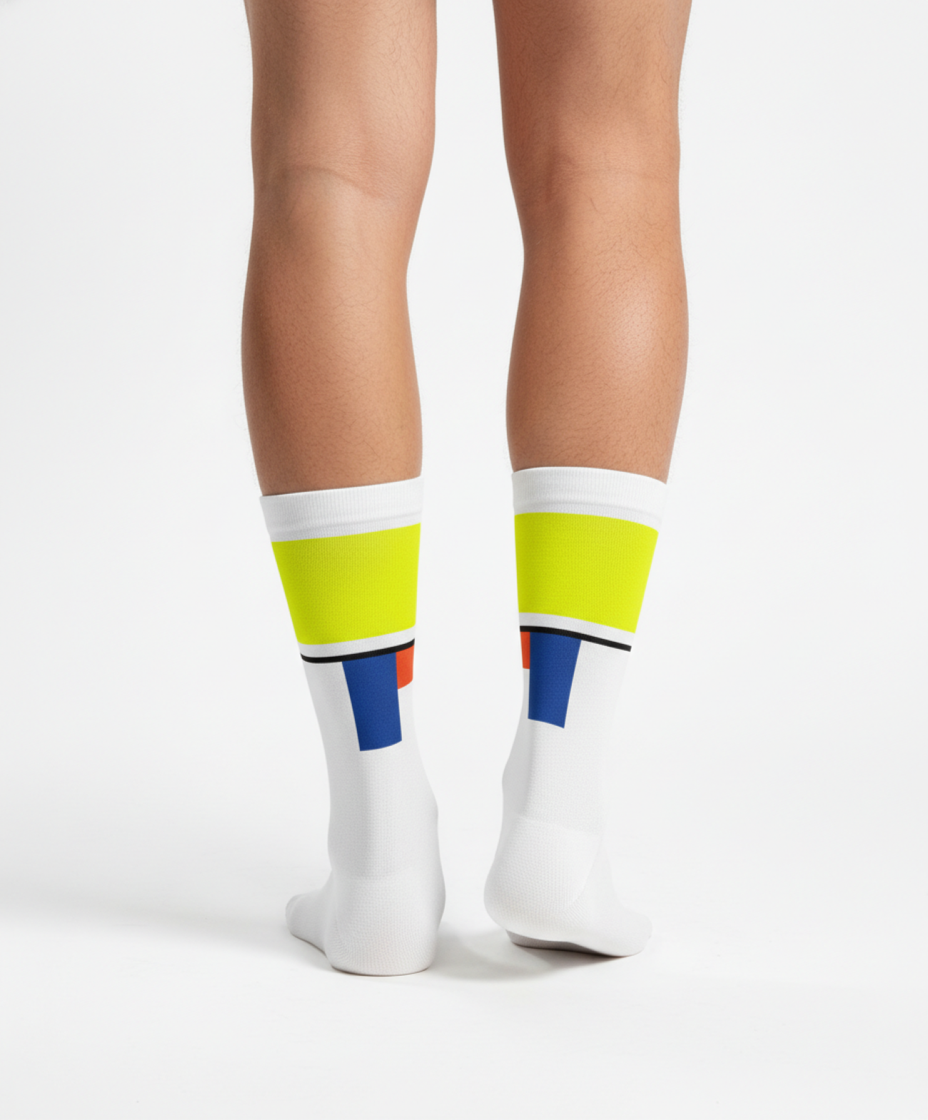 Weiße Radsocken mit neongelbem Bündchen und grafischen Farbdetails in Blau und Orange, getragen von hinten an den Unterschenkeln einer Person vor hellem Studiohintergrund.