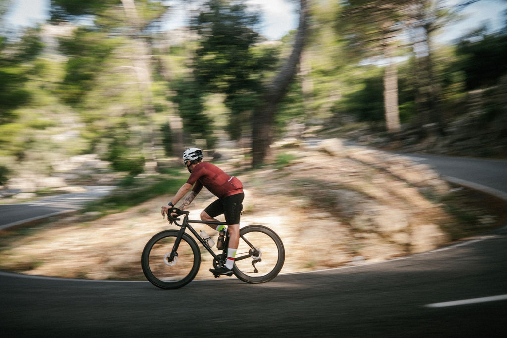 Rennradfahrer der um die Kurve fährt mit roten Trikot und einen schwarzen bib short